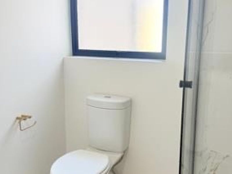 A clean and modern bathroom featuring a white toilet, a glass-enclosed shower, and neutral wall tiling.