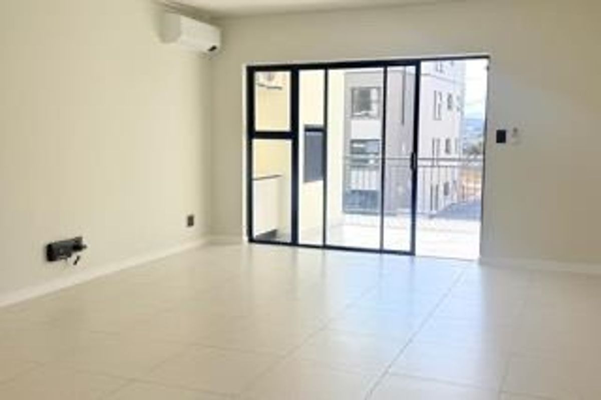 A bright, empty living room featuring tiled flooring, a wall-mounted air conditioning unit, and large sliding glass doors leading to a balcony.