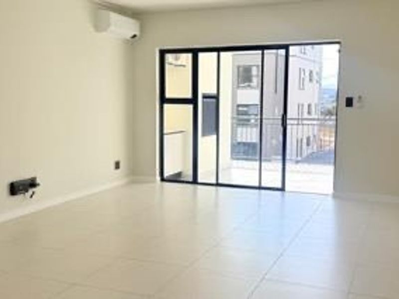 A bright, empty living room featuring tiled flooring, a wall-mounted air conditioning unit, and large sliding glass doors leading to a balcony.