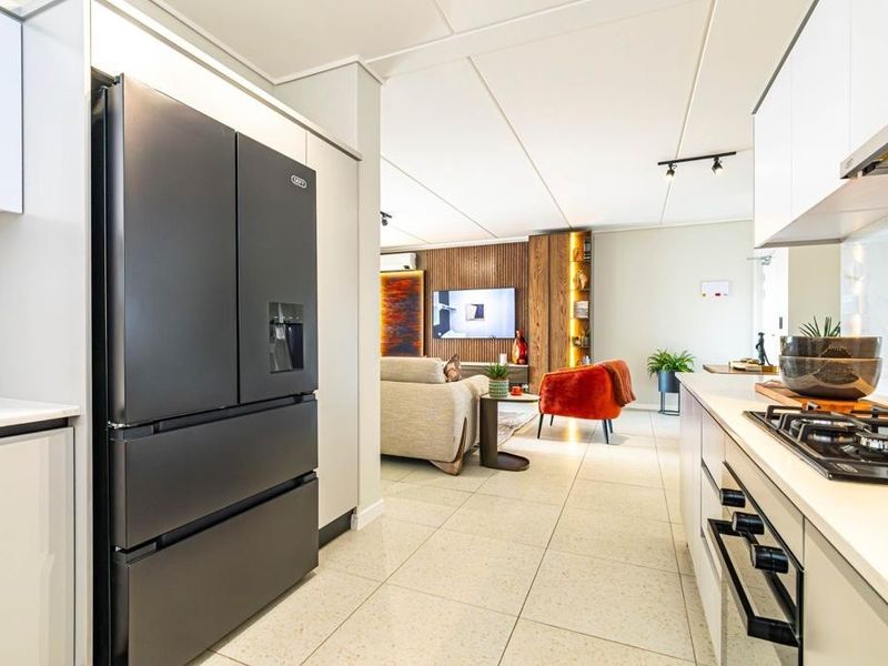 Modern open-plan kitchen and living area featuring sleek cabinetry, stone countertops, integrated appliances, and contemporary tiled flooring throughout.