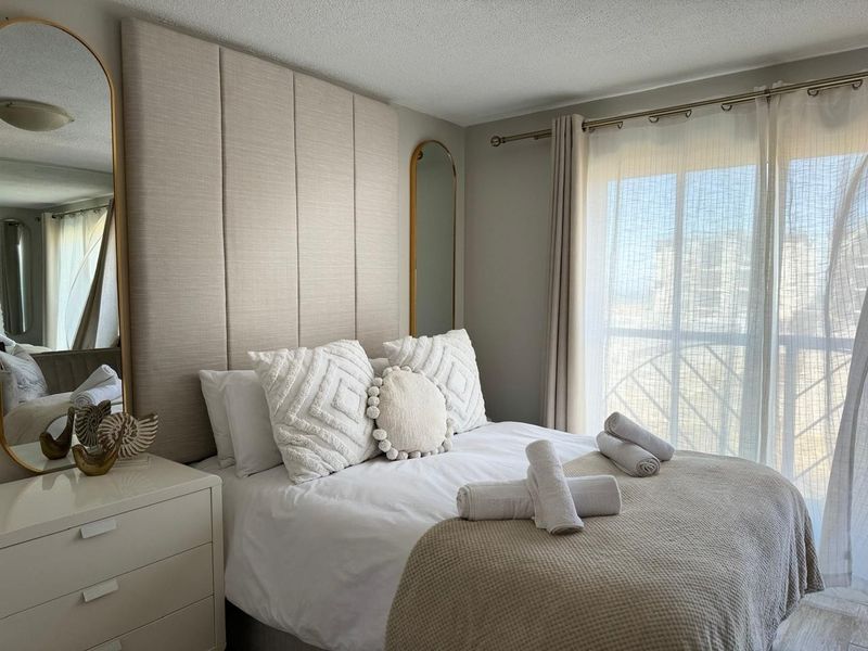 A well-maintained bedroom featuring a floor-to-ceiling upholstered headboard and a sliding glass door providing natural light and access to a balcony.