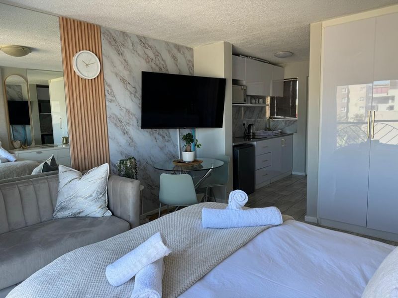 A modern open-plan studio apartment featuring a kitchenette, built-in wardrobe, and stylish marble-effect feature wall with integrated television.