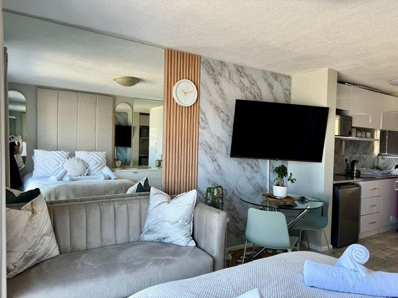Open-plan studio apartment featuring a mirrored wall, marble-effect accent wall with timber detailing, and a compact kitchen area with modern cabinetry.