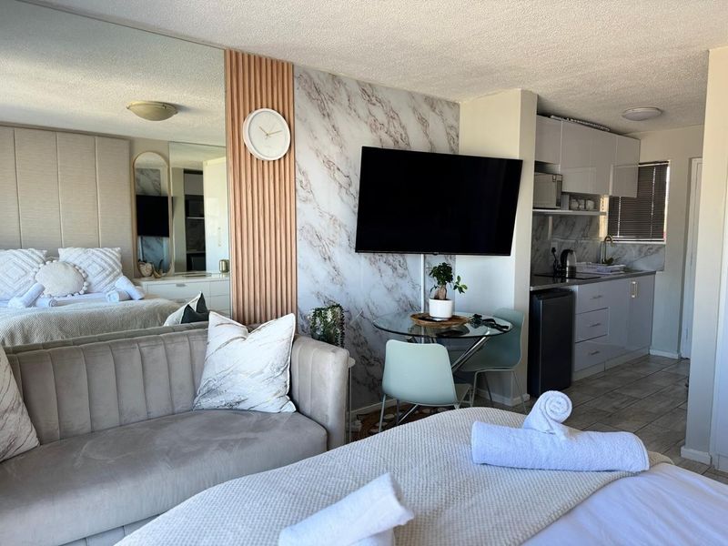 Open-plan studio apartment featuring a kitchenette, marble-effect feature wall, slatted timber accents, and a mirrored wall, creating a modern and functional living space.