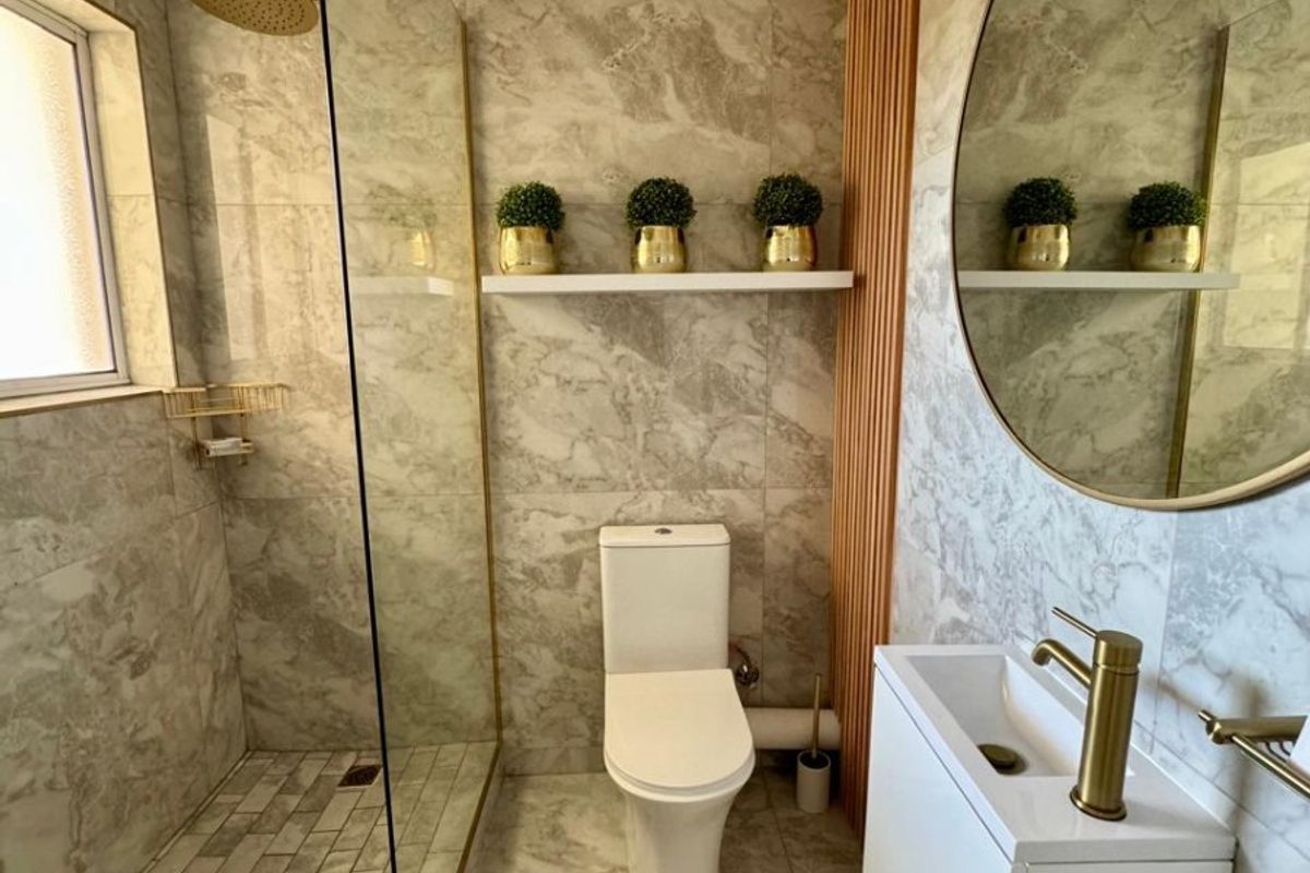 Modern bathroom featuring marble-effect tiling, a walk-in shower with brass fixtures, a wall-mounted vanity, and a stylish slatted wood accent wall.