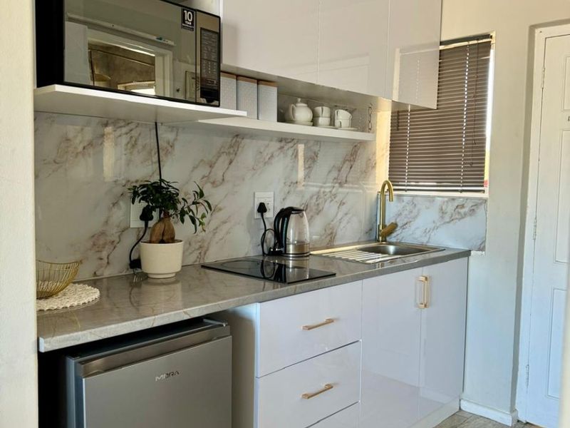 A compact, modern kitchen featuring white high-gloss cabinetry, marble-effect splashbacks, stone-look countertops, and brass hardware, complemented by tiled flooring.
