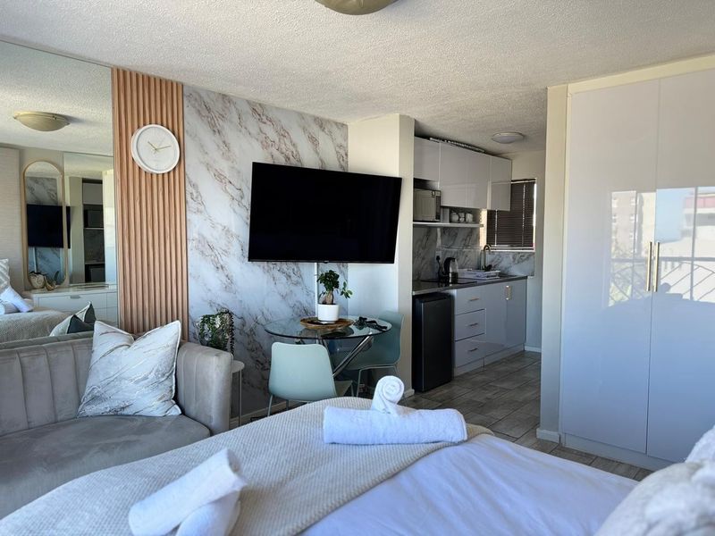 A modern open-plan studio apartment featuring a kitchenette, built-in wardrobe, and stylish marble-effect wall accents with integrated slatted wood detailing.