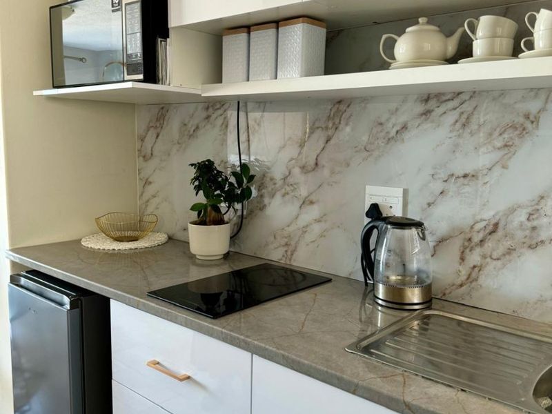 Modern compact kitchen featuring white gloss cabinetry, marble-look splashback, stone-look countertop, induction hob, and integrated microwave.