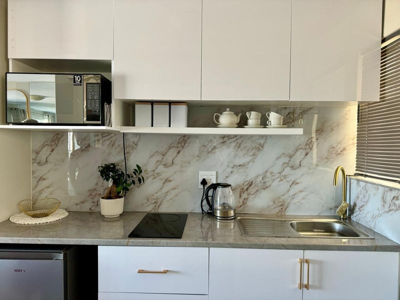 Modern kitchen featuring white cabinetry, marble-look splashback, stone-look countertop, induction cooktop, and a sleek brass-finish faucet.