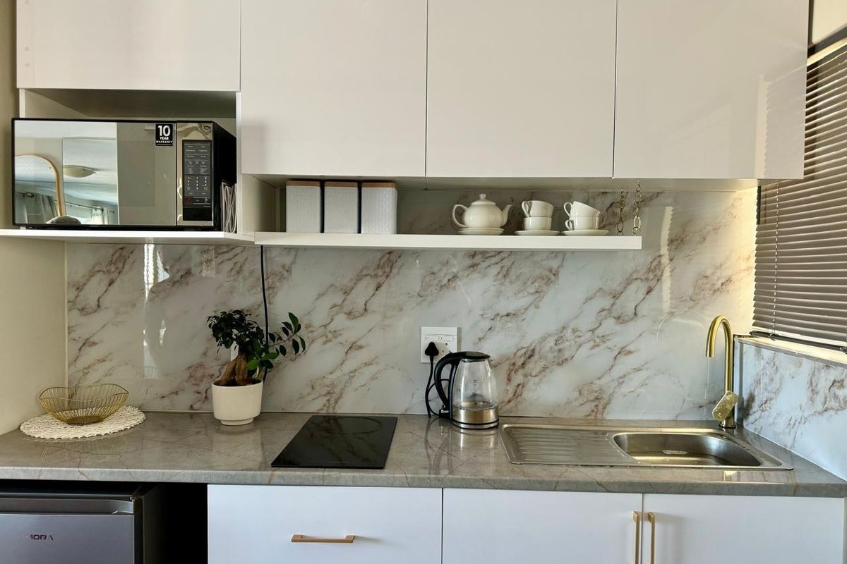 Modern kitchen featuring white cabinetry, marble-look splashback, stone-look countertop, induction cooktop, and a sleek brass-finish faucet.