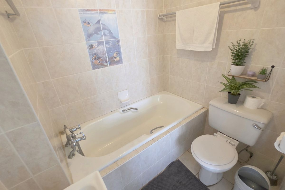 A functional bathroom featuring a built-in bathtub with decorative tile accents, a standard toilet, and neutral wall tiling.
