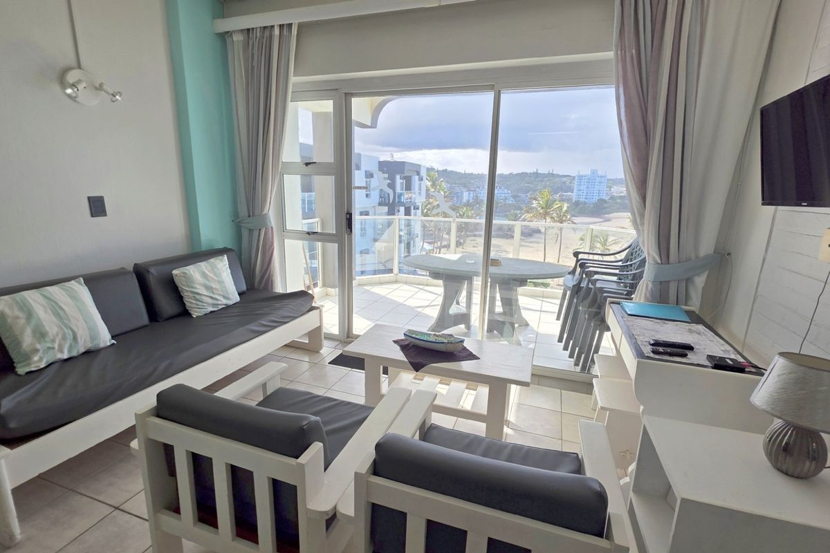 A bright living room featuring tiled flooring and a large sliding glass door that provides direct access to a private balcony with coastal views.