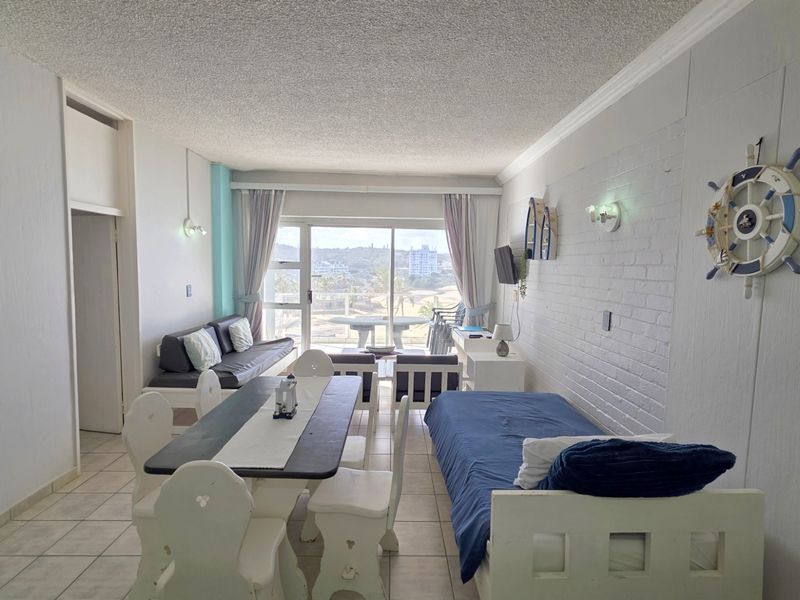Open-plan living and dining area featuring tiled floors, an exposed brick feature wall, and large sliding doors leading to a balcony with coastal views.