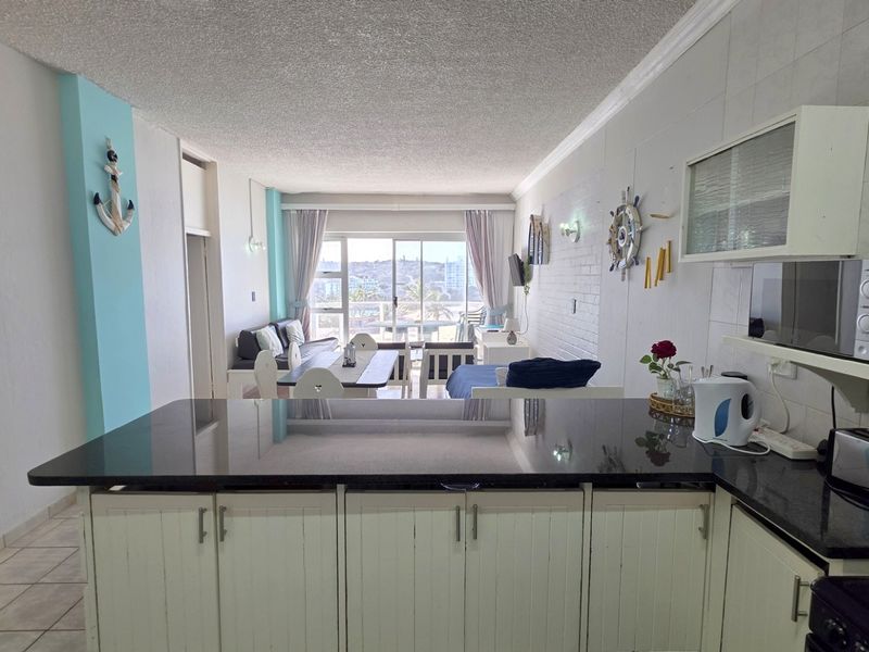 Open-plan living and kitchen area featuring granite countertops, white cabinetry, and direct access to a balcony with natural light.