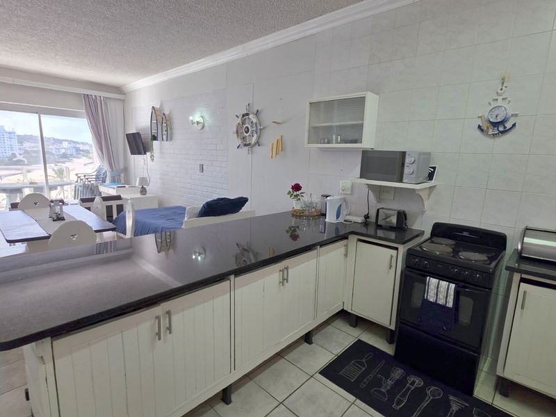 Open-plan kitchen and living area featuring granite countertops, white cabinetry, and direct access to a balcony with coastal views.