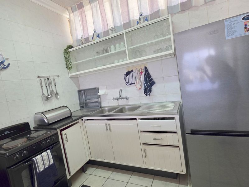 A functional kitchen featuring white cabinetry, tiled backsplash, double sink, and tiled flooring, offering a practical layout for daily meal preparation.