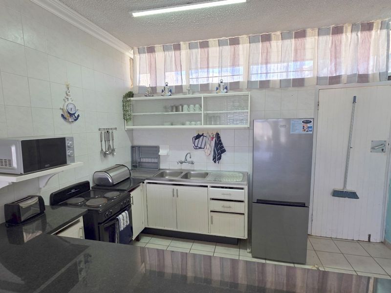 A functional kitchen featuring tiled walls, built-in cabinetry, a double sink, and an electric stove, offering a practical layout with potential for modern updates.