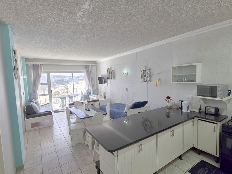 Open-plan living and kitchen area featuring tiled floors, granite countertops, and direct access to a balcony with coastal views.