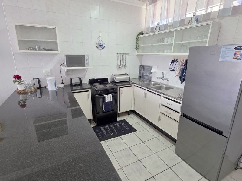 A functional kitchen featuring granite countertops, ample built-in cabinetry, a double basin sink, and tiled flooring, offering a practical layout for daily use.