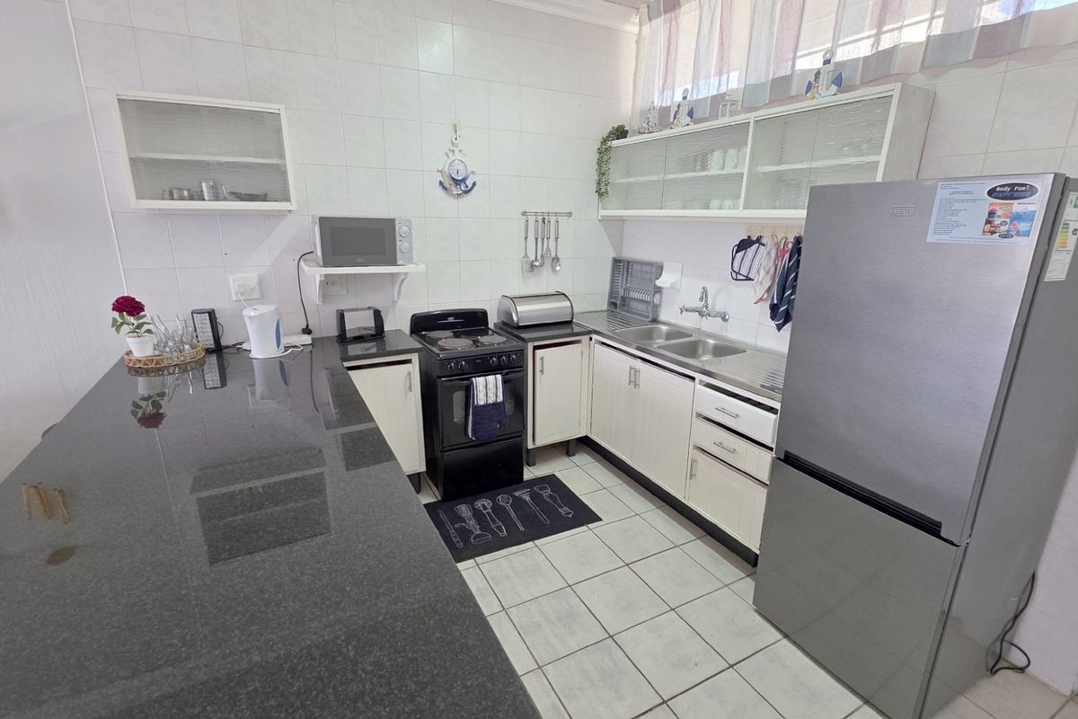 A functional kitchen featuring granite countertops, ample built-in cabinetry, a double basin sink, and tiled flooring, offering a practical layout for daily use.