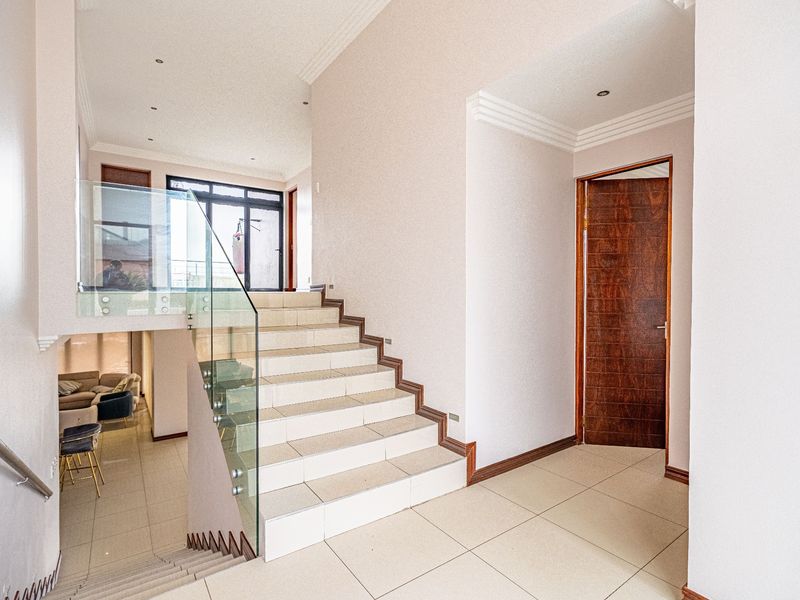Spacious entrance hall featuring a tiled staircase with a modern glass balustrade, recessed lighting, and elegant crown molding.