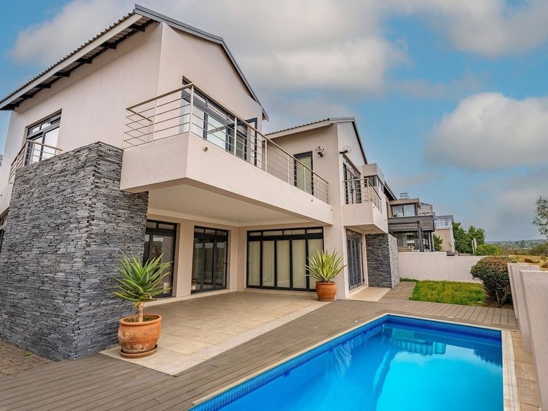 Modern double-story residence featuring a rear patio, timber decking, swimming pool, and stone-clad architectural accents with upper-level balconies.