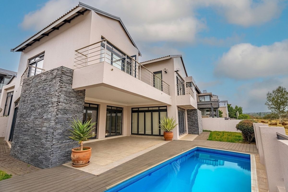 Modern double-story residence featuring a rear patio, timber decking, swimming pool, and stone-clad architectural accents with upper-level balconies.