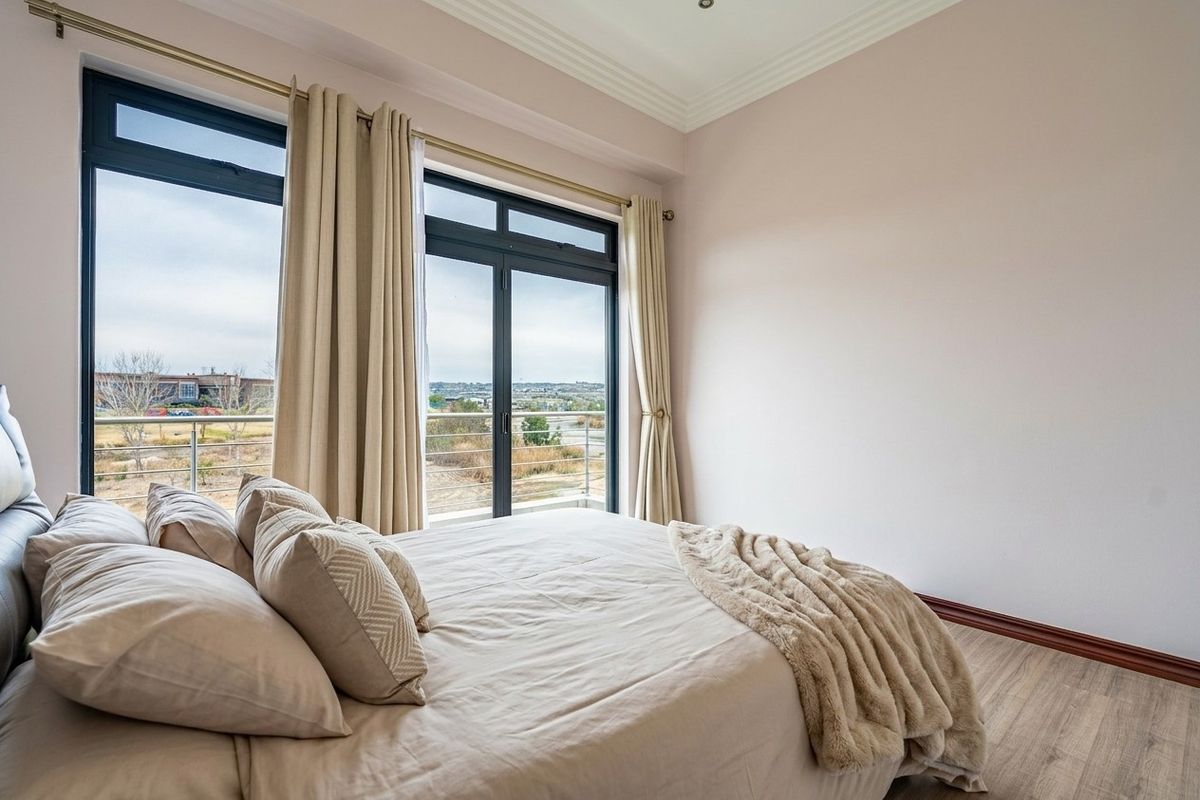 A bright bedroom featuring laminate flooring, elegant cove ceiling molding, and large sliding glass doors that open onto a private balcony with scenic views.