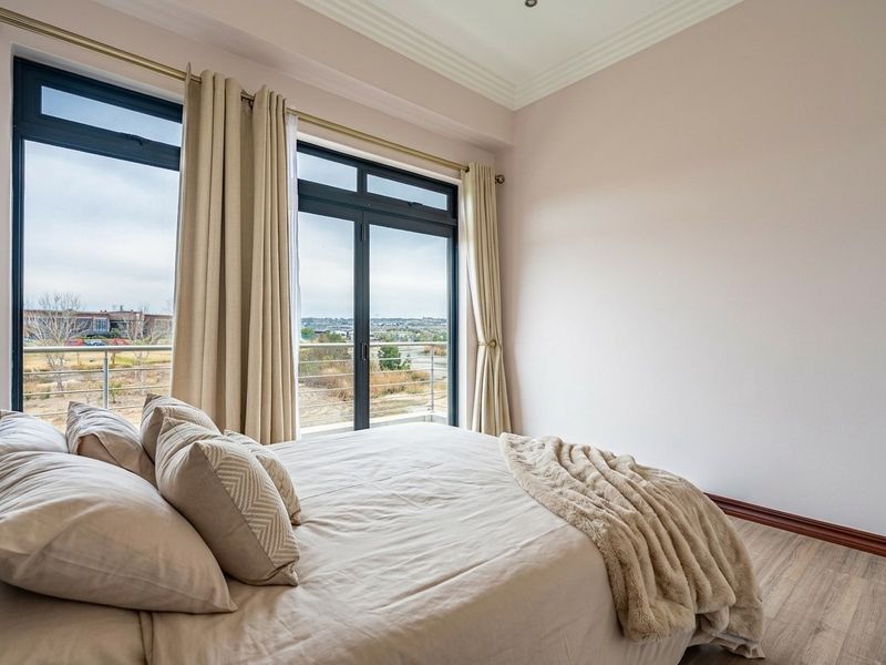 A bright bedroom featuring laminate flooring, elegant cove ceiling molding, and large sliding glass doors that open onto a private balcony with scenic views.