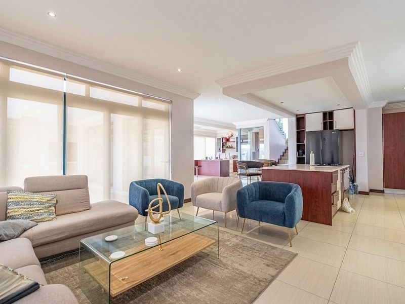 Spacious open-plan living area featuring a modern kitchen with a central island, tiled flooring, and recessed lighting, seamlessly connecting to the lounge space.