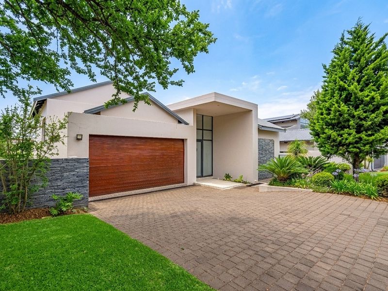 Modern front elevation featuring a paved driveway, double garage, stone-clad accents, and a well-maintained landscaped garden.