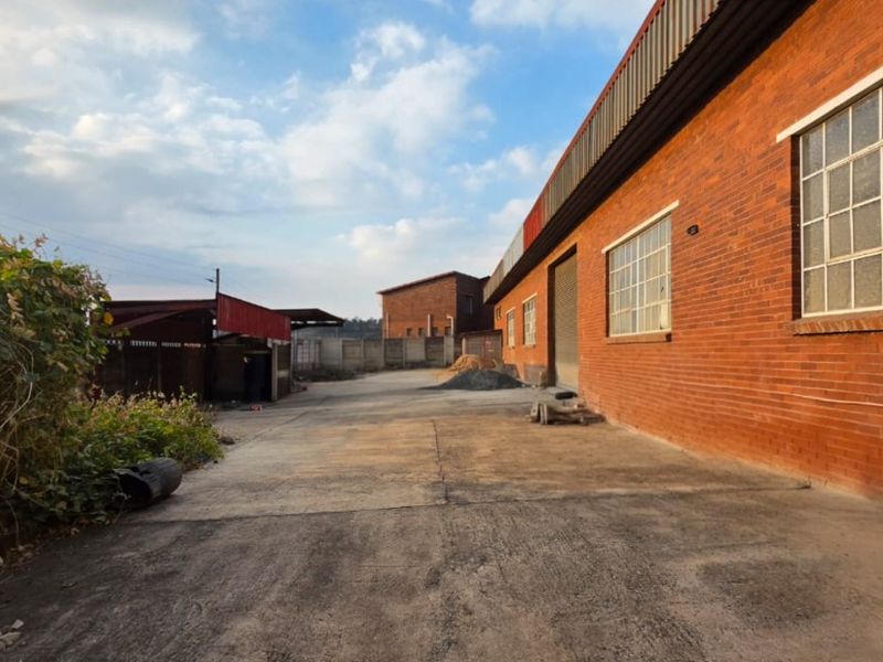 Rear exterior view of an industrial property featuring a brick facade, concrete yard space, and secure perimeter walling.