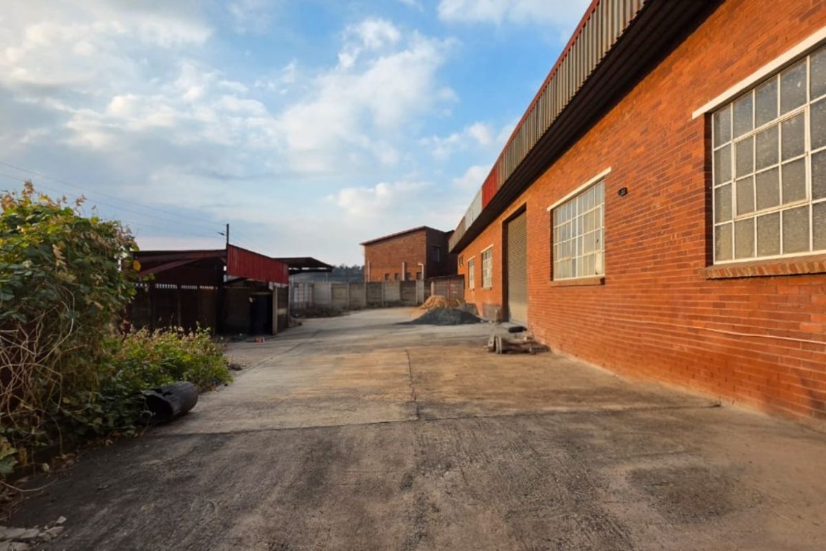 Rear exterior view of an industrial property featuring a brick facade, concrete yard space, and secure perimeter walling.