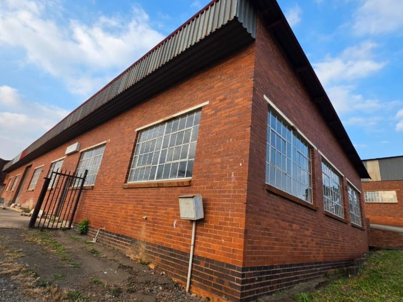 Exterior view of an industrial brick building featuring steel-framed windows and corrugated metal roof detailing.