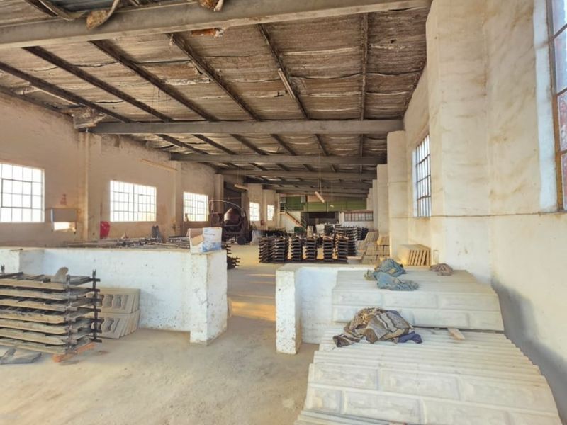 Spacious industrial utility area featuring exposed steel roof trusses, concrete flooring, and large steel-framed windows, suitable for manufacturing or storage operations.