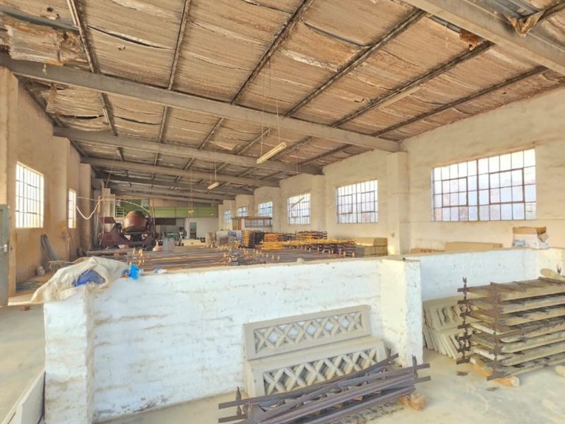 Spacious industrial utility area featuring exposed steel roof trusses, concrete flooring, and large steel-framed windows, suitable for workshop or storage use.