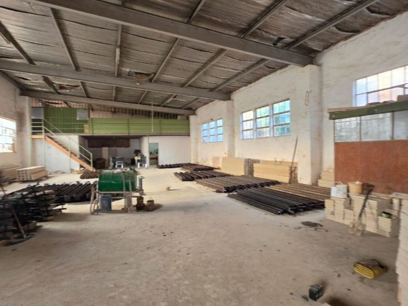 Spacious industrial warehouse area featuring high ceilings with exposed steel trusses, a mezzanine level, and concrete flooring, suitable for various commercial or storage uses.