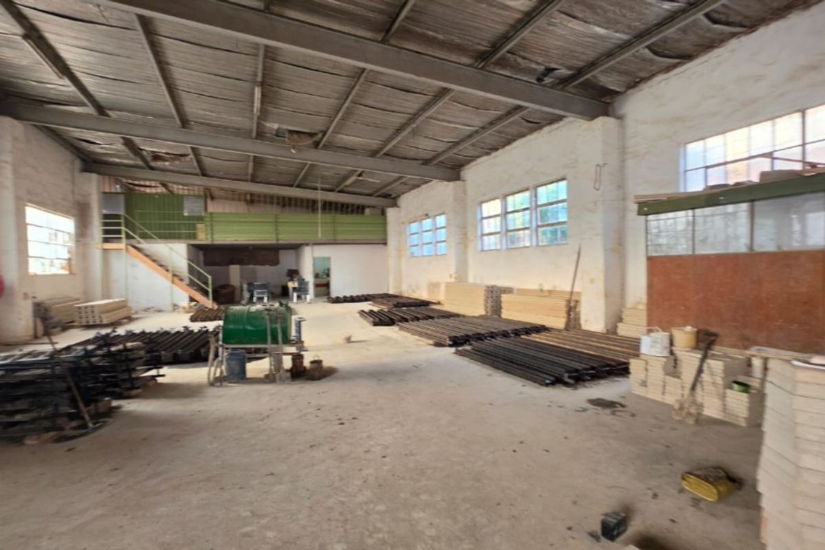 Spacious industrial warehouse area featuring high ceilings with exposed steel trusses, a mezzanine level, and concrete flooring, suitable for various commercial or storage uses.