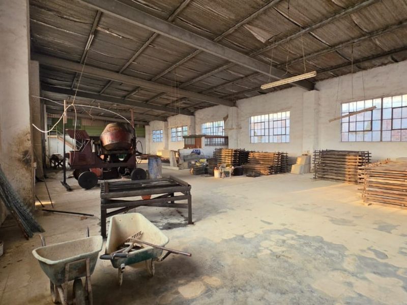 Spacious industrial utility area featuring high ceilings, exposed roof structure, large steel-framed windows, and durable concrete flooring, suitable for workshop or storage use.