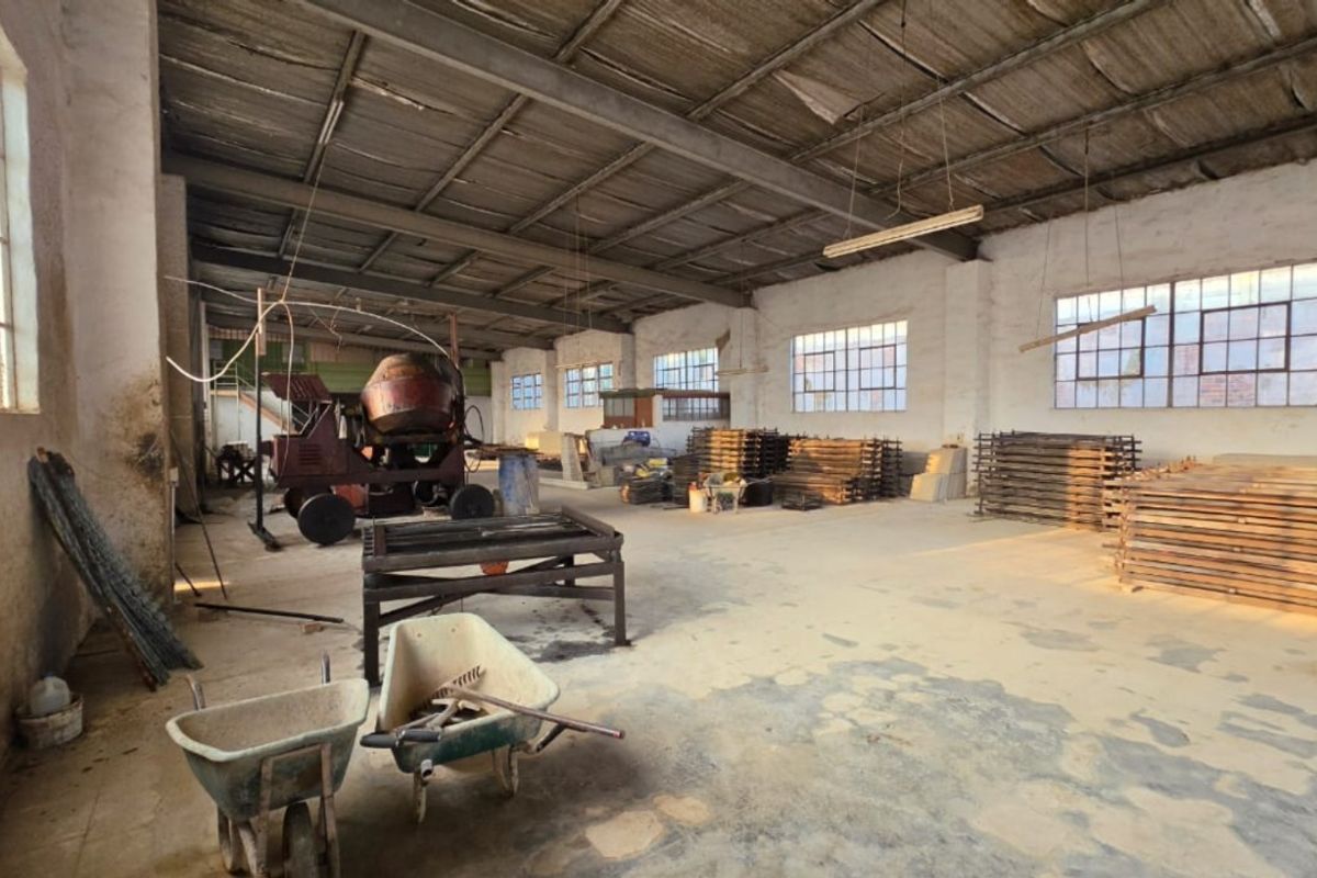 Spacious industrial utility area featuring high ceilings, exposed roof structure, large steel-framed windows, and durable concrete flooring, suitable for workshop or storage use.