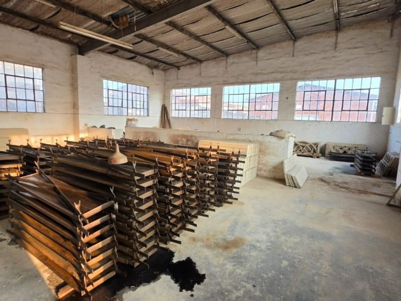 Spacious industrial utility area featuring exposed steel roof trusses, large steel-framed windows, and durable concrete flooring, suitable for workshop or storage use.
