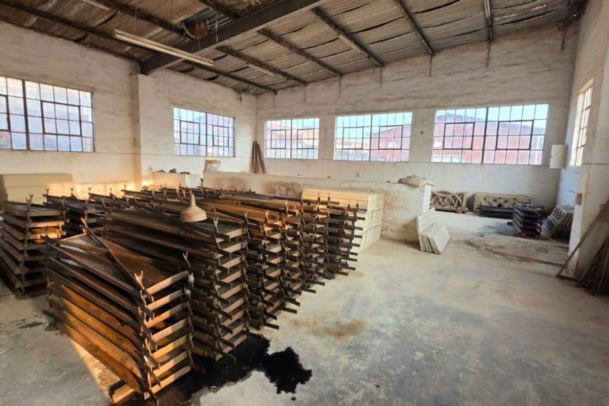 Spacious industrial utility area featuring exposed steel roof trusses, large steel-framed windows, and durable concrete flooring, suitable for workshop or storage use.