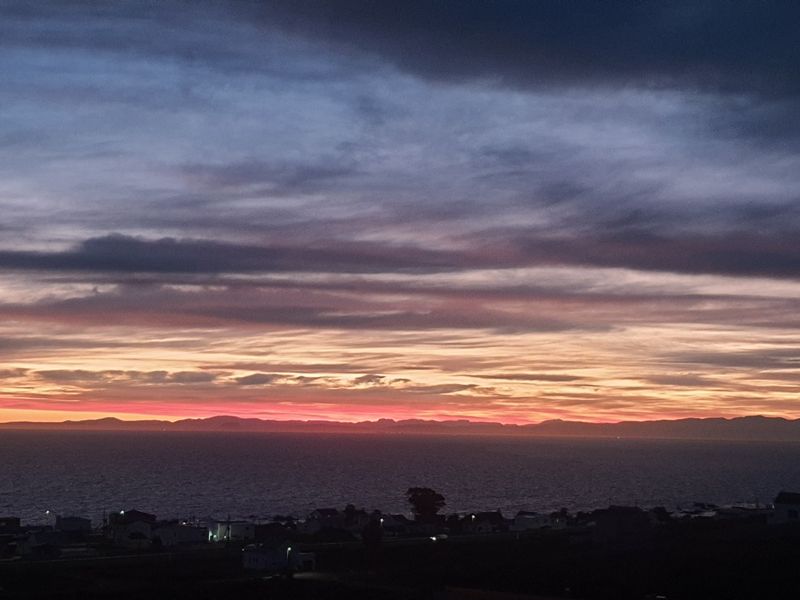 A scenic sunset view overlooking the ocean and distant coastline, showcasing the natural landscape and horizon.