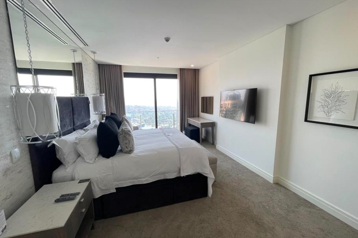 A modern, well-maintained bedroom featuring neutral carpeting, mirrored wall accents, and large sliding glass doors providing access to a balcony with city views.