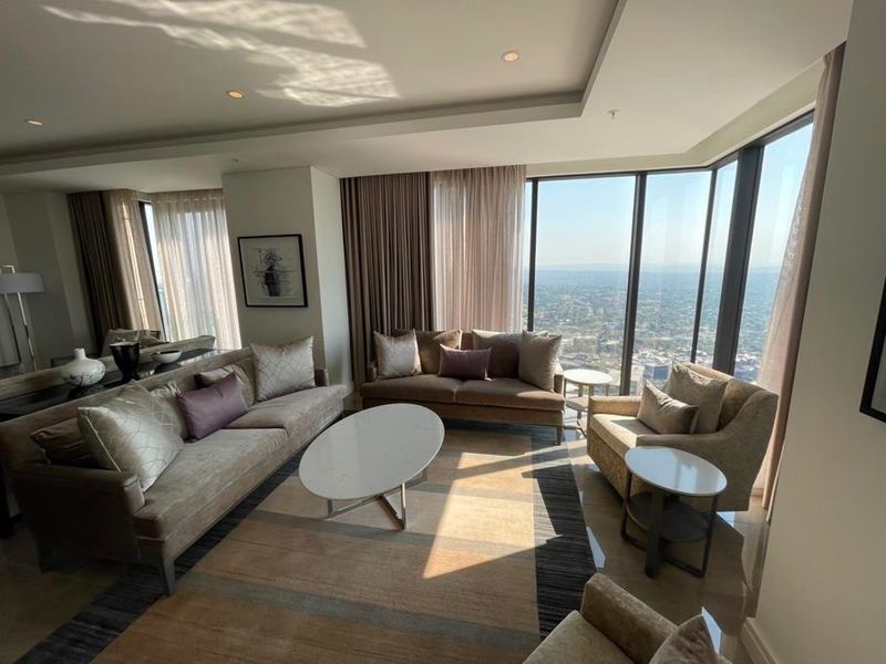 A bright, modern living room featuring floor-to-ceiling windows with expansive city views, recessed ceiling lighting, and high-quality tiled flooring.