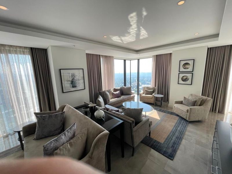 Spacious living room featuring floor-to-ceiling windows with panoramic views, recessed ceiling lighting, and high-quality stone flooring in a modern apartment setting.