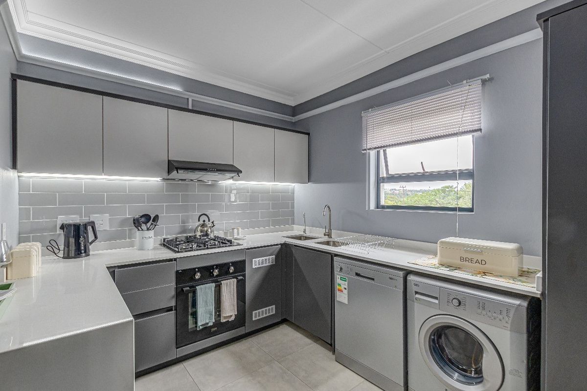 Modern kitchen featuring sleek grey cabinetry, quartz countertops, subway tile backsplash, integrated gas hob, oven, and under-cabinet lighting.