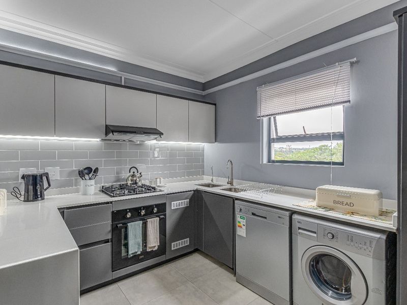 Modern kitchen featuring sleek grey cabinetry, quartz countertops, subway tile backsplash, integrated gas hob, oven, and under-cabinet lighting.