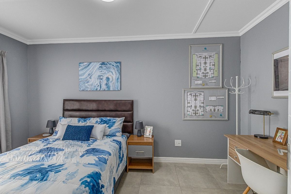A well-maintained bedroom featuring neutral grey walls, tiled flooring, and classic crown molding, providing a clean and comfortable living space.