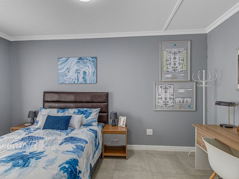 A well-maintained bedroom featuring neutral grey walls, tiled flooring, and classic crown molding, providing a clean and comfortable living space.
